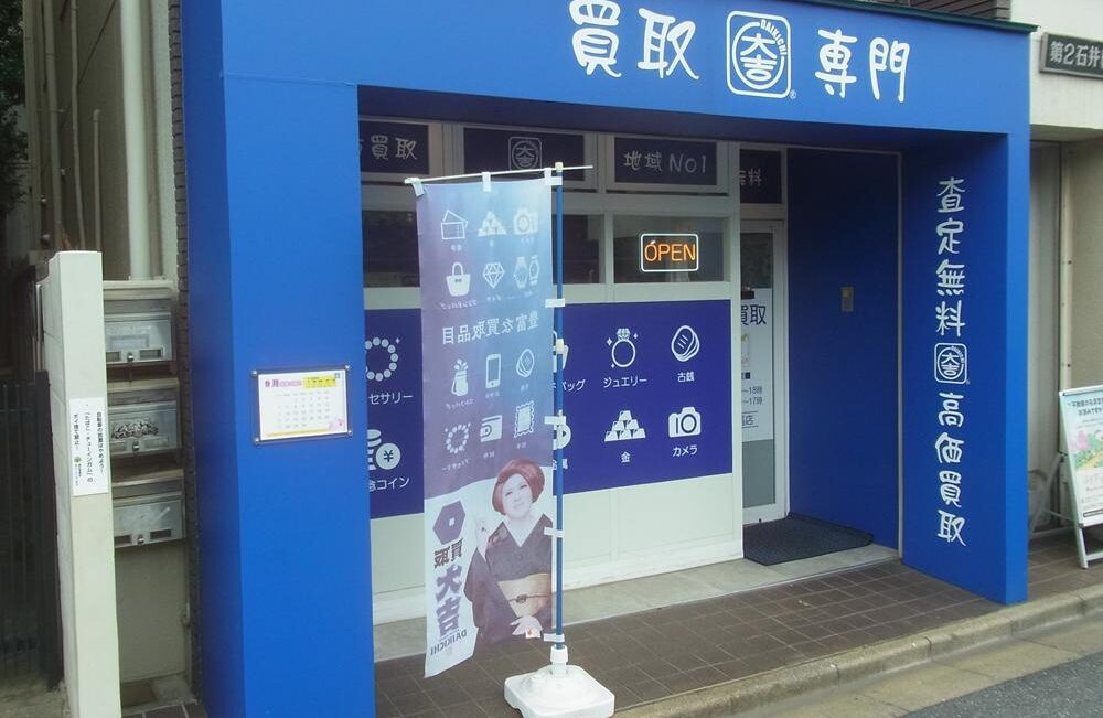 shop01 Blue storefront in Japan with kanji signage, glass doors, and an 'OPEN' sign; a tall promotional banner stands outside.